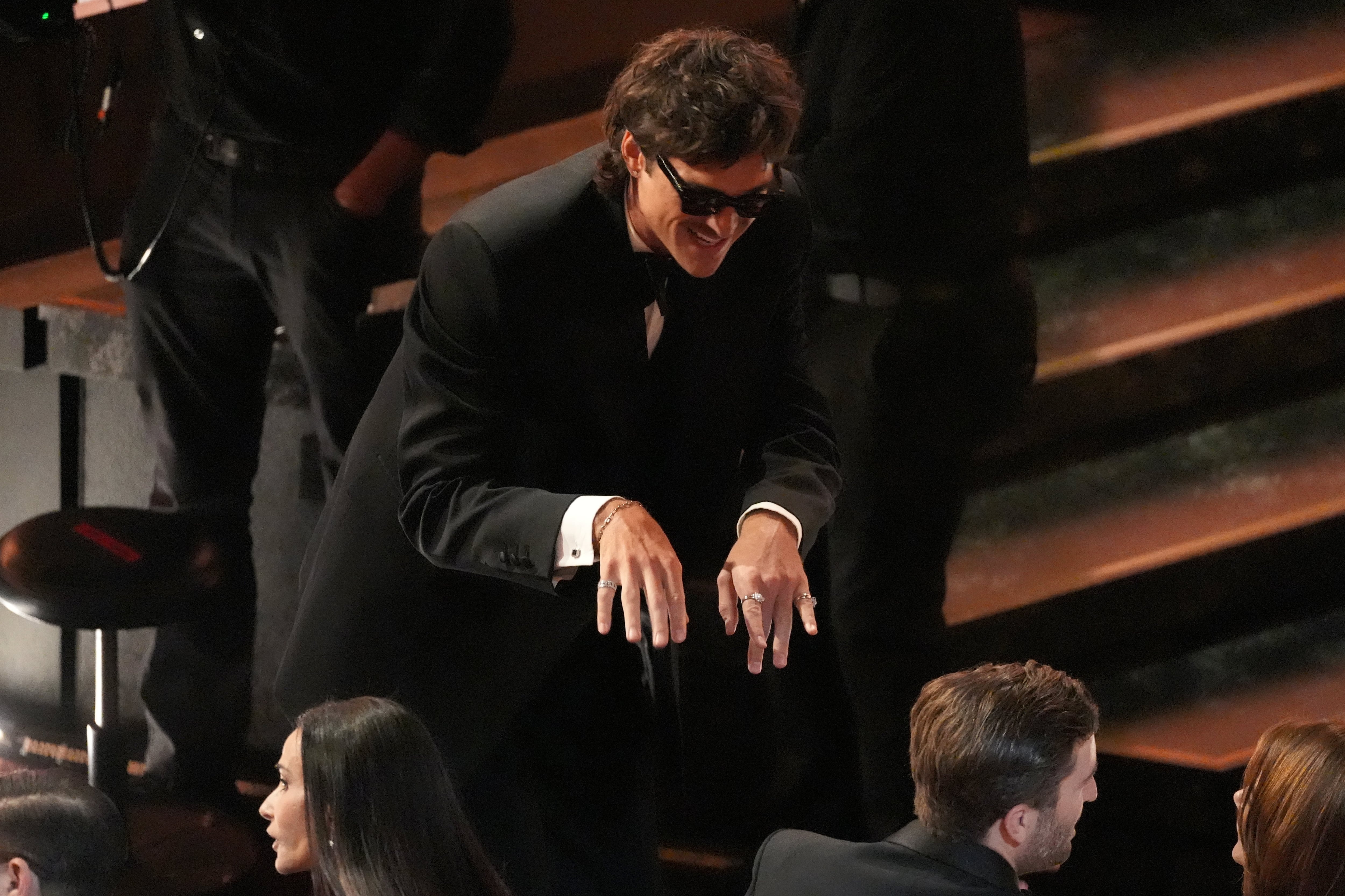 Vestido de negro, con anteojos de sol y varios anillos completando el look, Jacob Elordi se mostró divertido sonriendo mientras se preparaba para tomar asiento en la sala